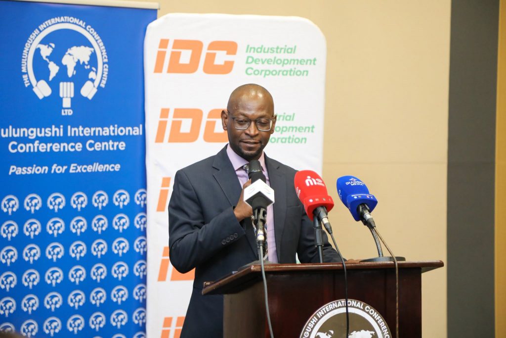 A speaker delivers remarks beside the MICC and IDC banners
