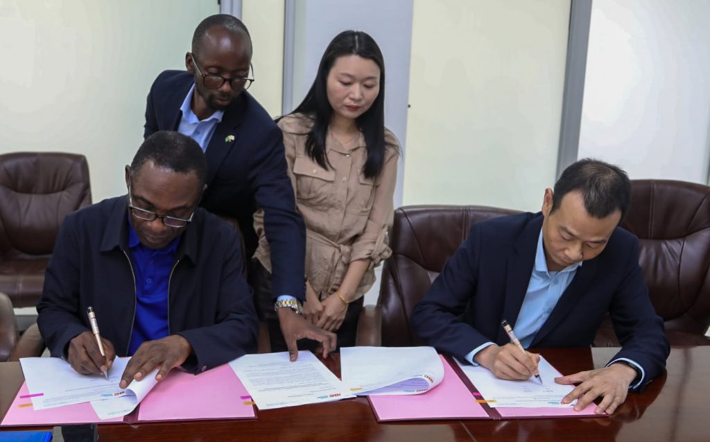 IDC and Rong Xing representatives sign the letter of intent as a colleague stands behind them.