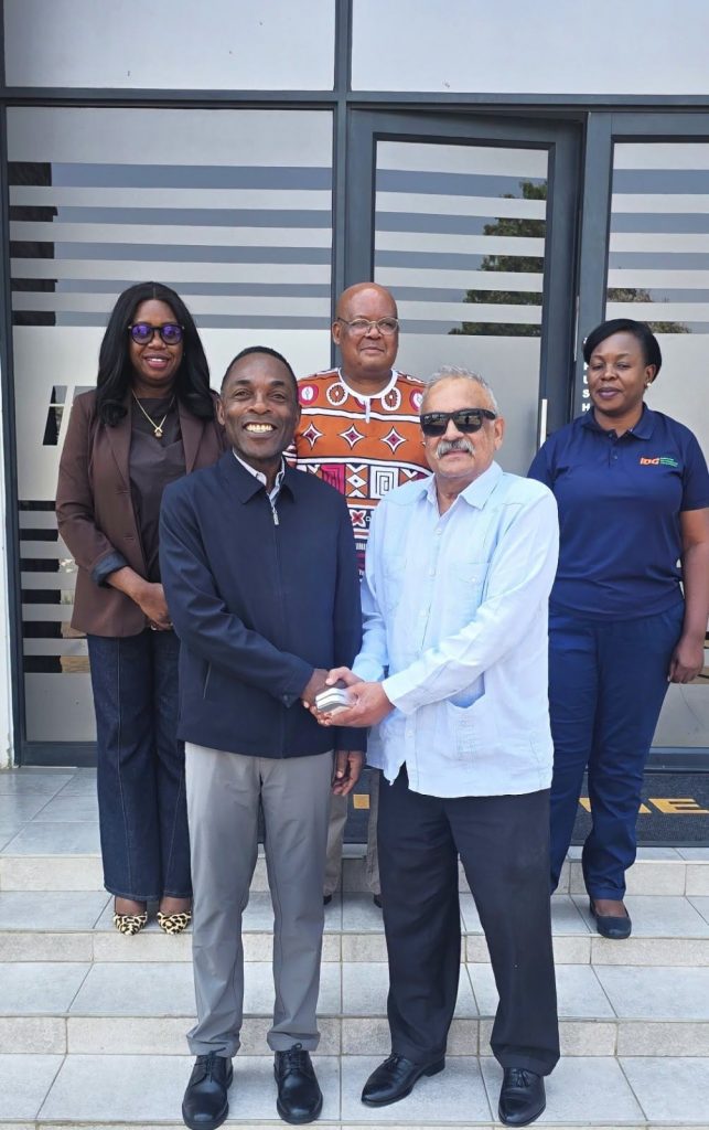 Mr. Cornwell Muleya and High Commissioner Saad Cachalia shake hands outside IDC offices, joined by members of both delegations.